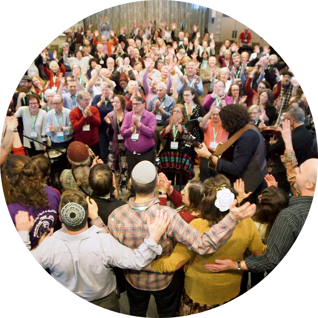 Image from people standing during a concert at a pervious Reconstructing Judaism convention.  Everyone is standing, clapping, raising hands in the air with a joyful look on their faces.